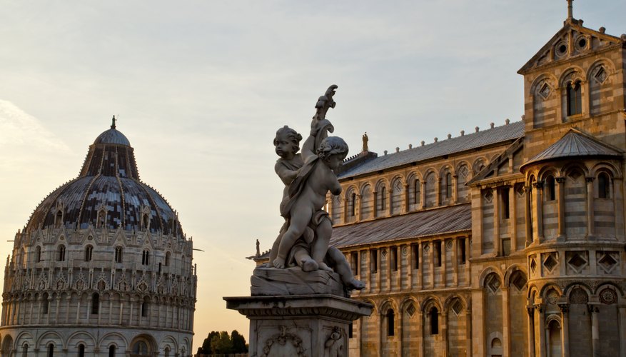 The top of the Leaning Tower of Pisa at sunset next to a statue and cathedral.