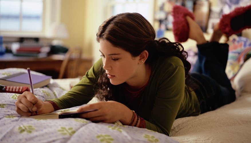 Teen writing while lying on her bed.