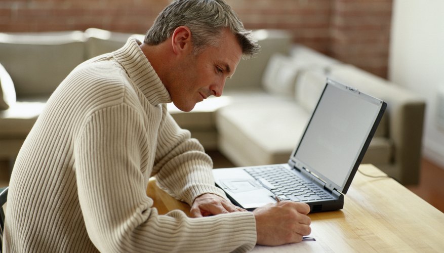 Man working on laptop from home while taking notes