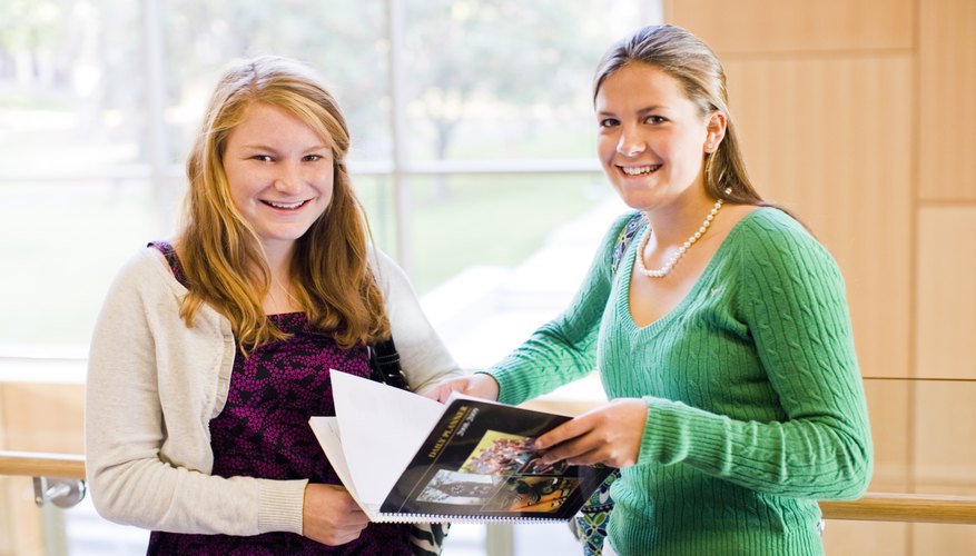 Two high school students looking through a book together.