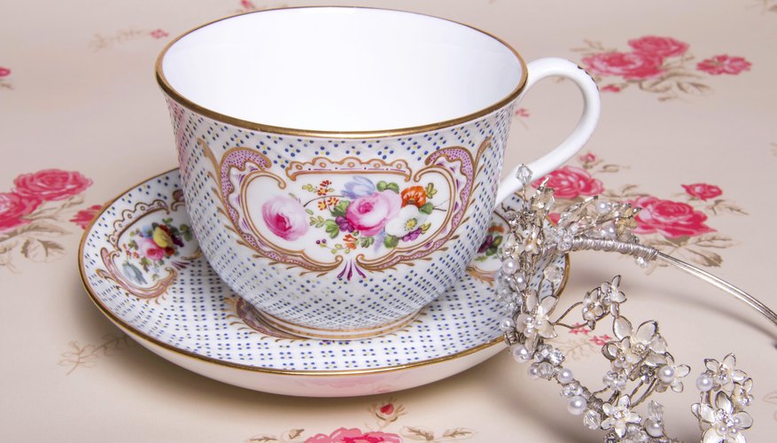 A close-up of a tiara leaning against a tea cup on a tablecloth.