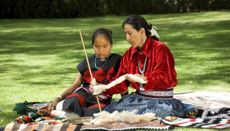 A Navajo woman teaches a young girl how to use a drop spindle to spin yarn.
