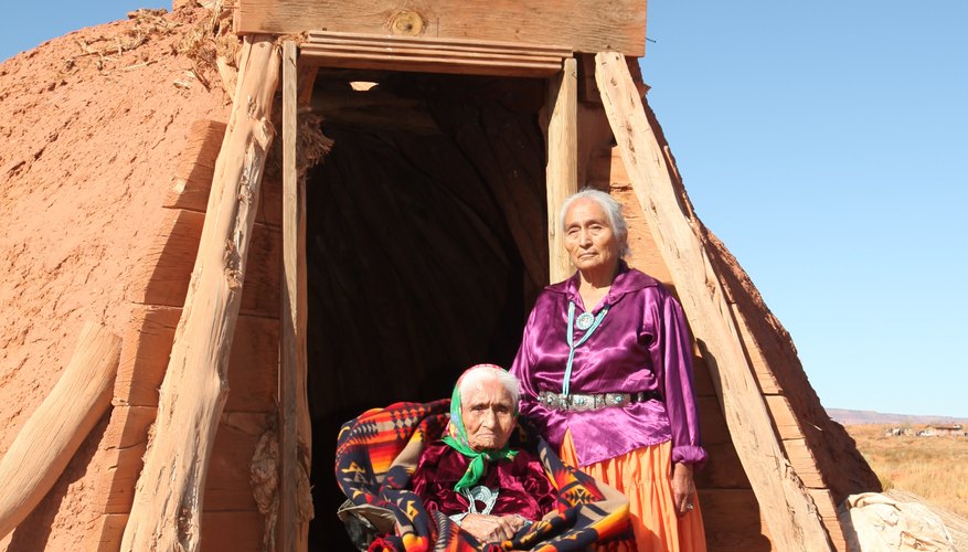 Two elderly Navajo women outside the entrance to a hut