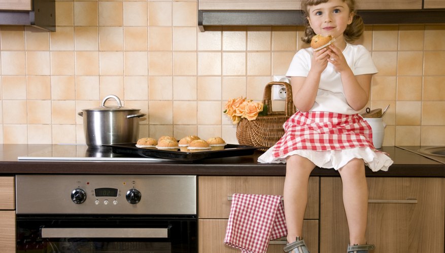 Young girl eating a muffin while sitting on a kitchen counter.