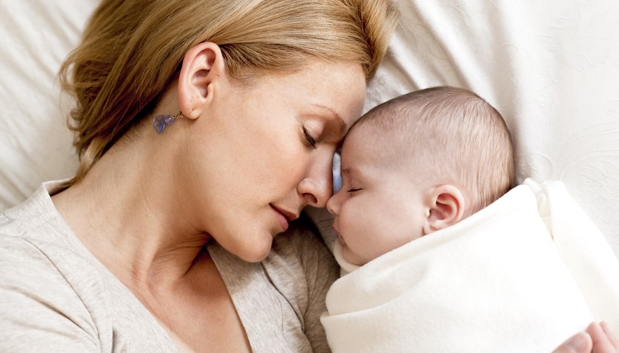 A mother holds her infant while lying in bed.