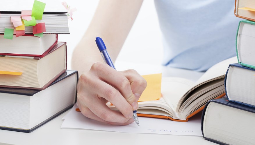 A woman writes with research books nearby.