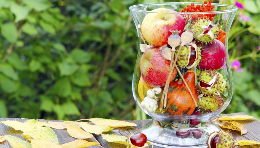 A glass vase filled with seasonal fruit and flowers.