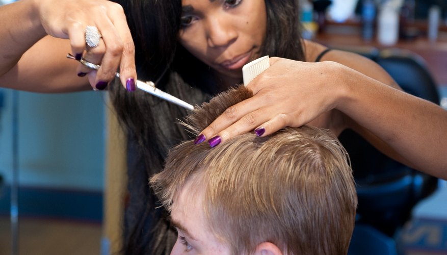 A cosmetologist cuts a young man's hair in a salon.