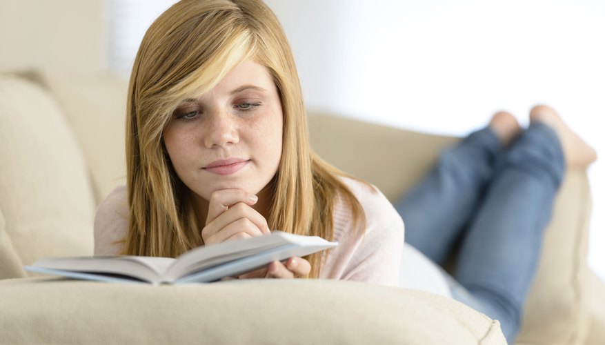 Teenager reading book on couch.