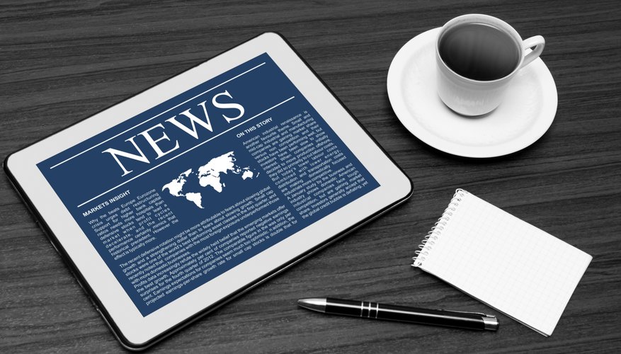 The news is on an e-reader next to a cup of coffee and pad of paper.