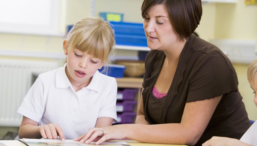 Teacher reading with young student at school table.