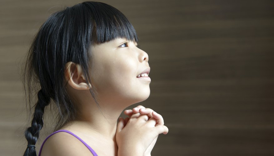 A young girl smiles with hands folded.