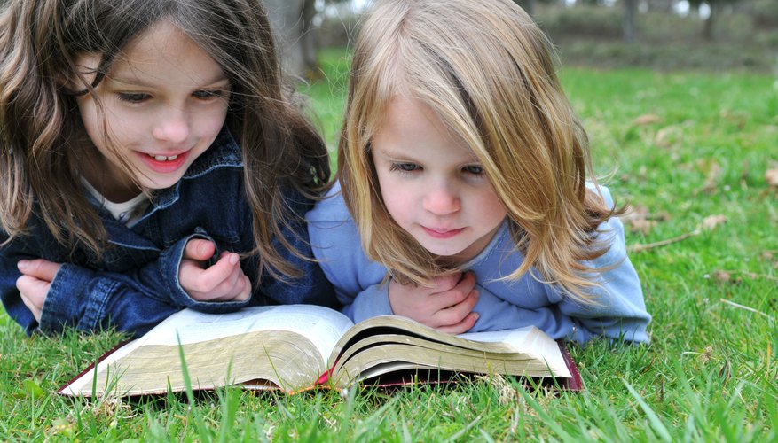 Two young girls reading the Bible on grass