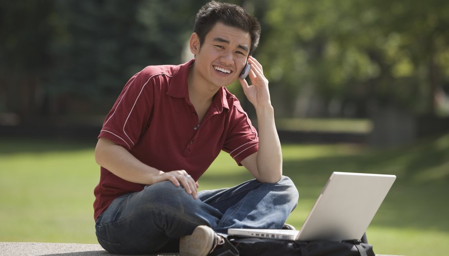 Student working on laptop while talking on cellphone.