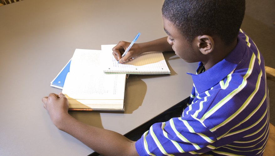 Student writing in notebook at table.