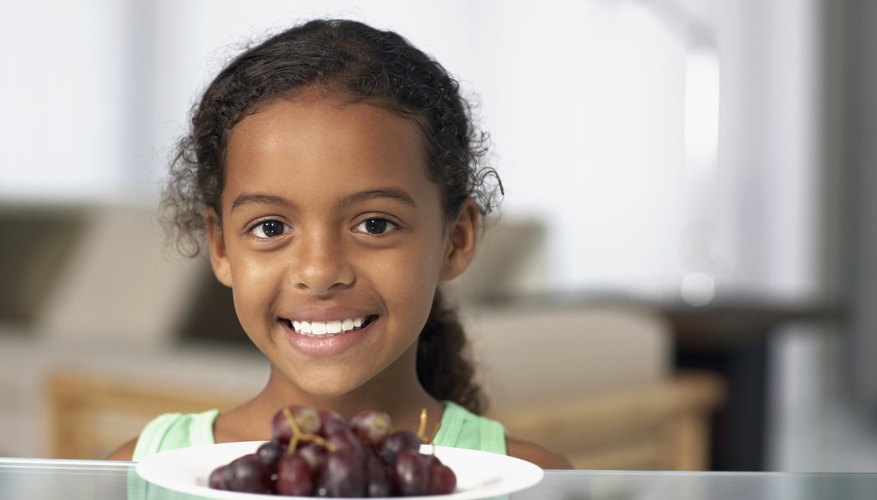 Smiling child behind small plate of grapes.
