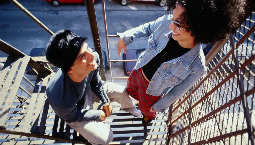 Two young adults hanging out on a fire escape outside of a city loft.