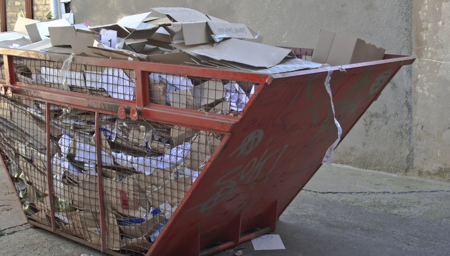 A large recycling receptacle on an urban sidewalk is filled with paper.