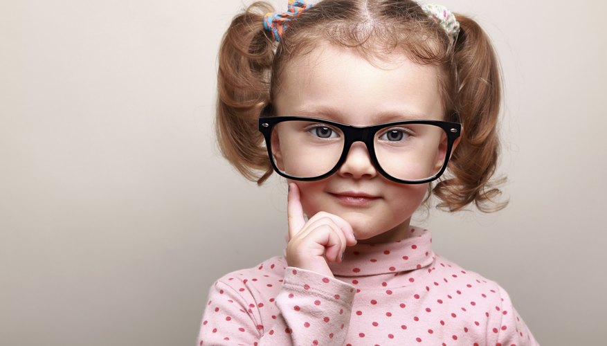 A little girl with pigtails wears glasses and ponders.