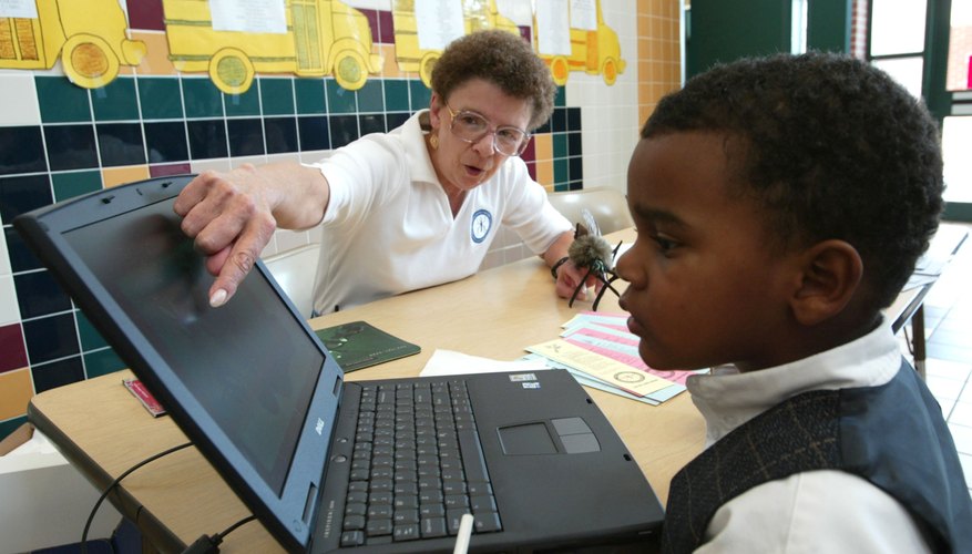 A woman shows a young boy how to use the computer.