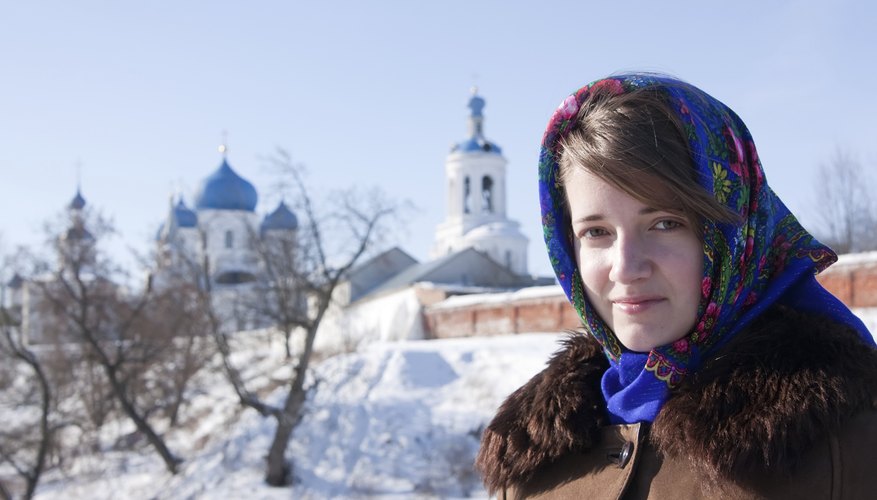 A woman wearing a fur-lined coat and a babushka tied around her face in the snow.