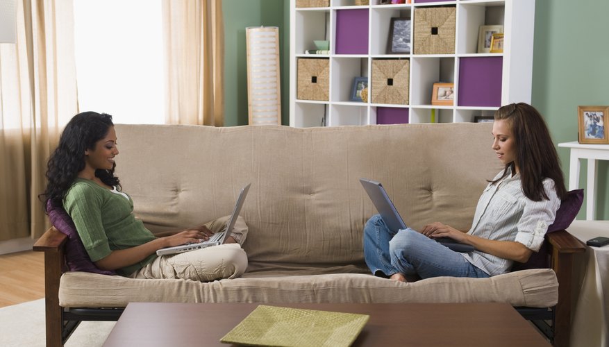 Two students working on laptops while sitting on couch.