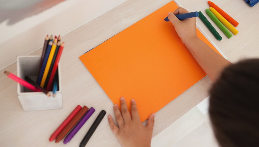An overhead view of a boy creating with paper and colored pencils.