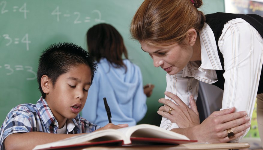 Teacher help young student with workbook in classroom