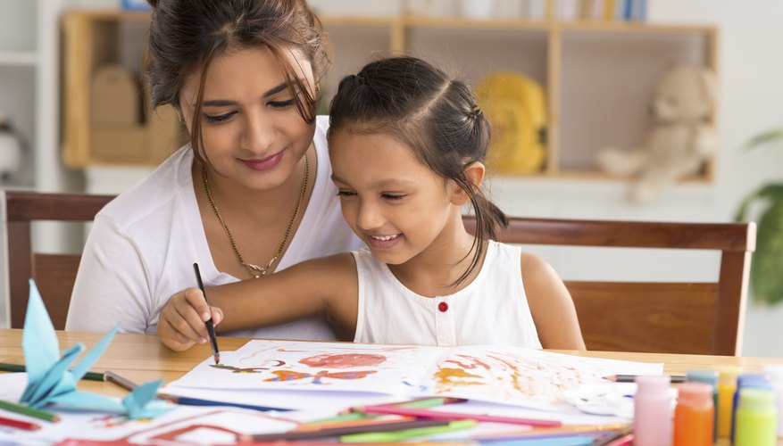 A mother assisting her daughter with an art project in a classroom.