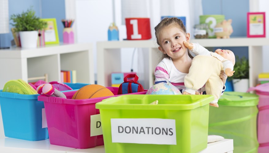 A young girl is bringing a doll to a donation bin at school.