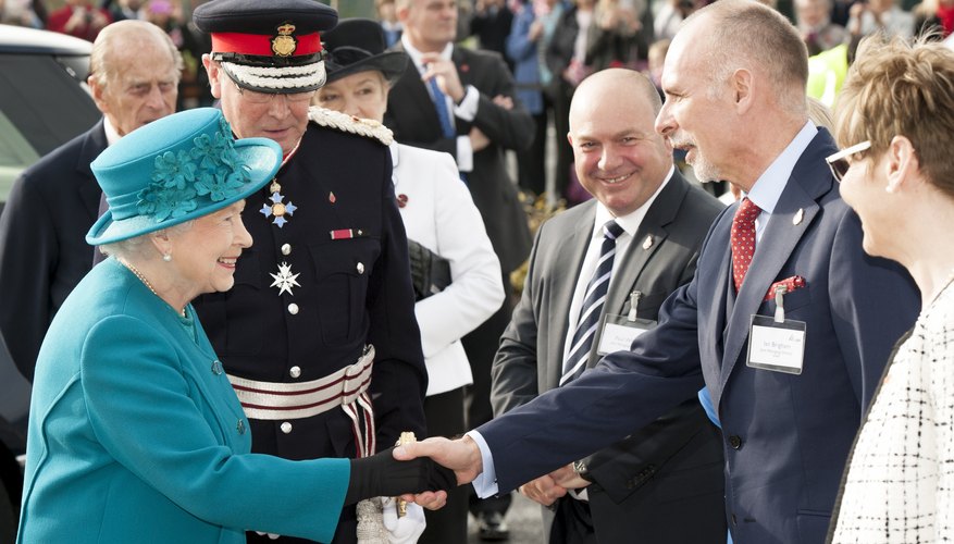 Queen Elizabeth smiles and shakes a man's hand.