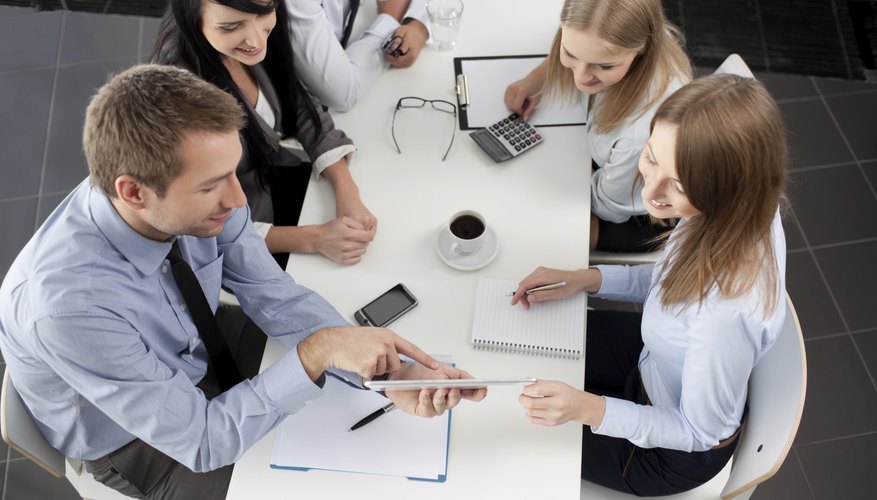 Young businesspeople are gathered around a table looking at papers and tablets.