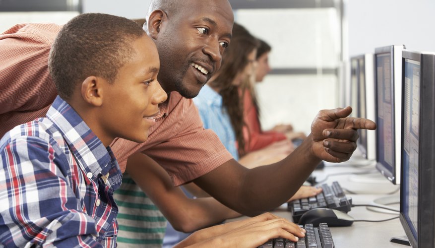High school students working at computers with help of teacher