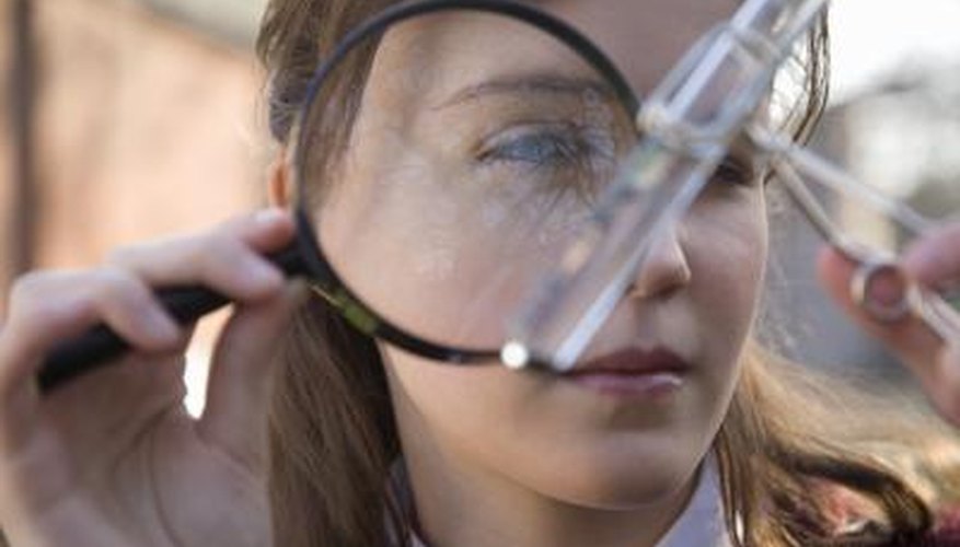 A girl looks at a test tube through a magnifying glass.
