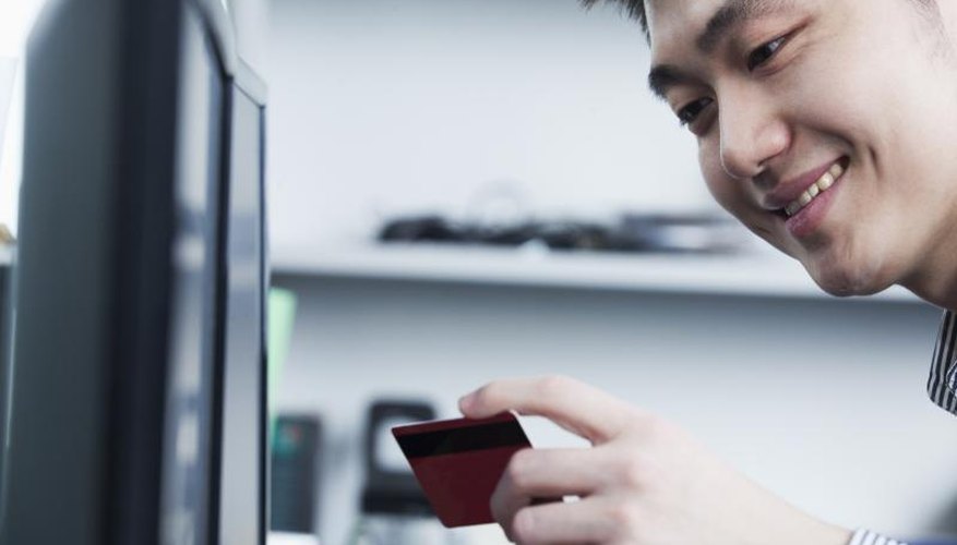 A man is holding his credit card in front of a computer.
