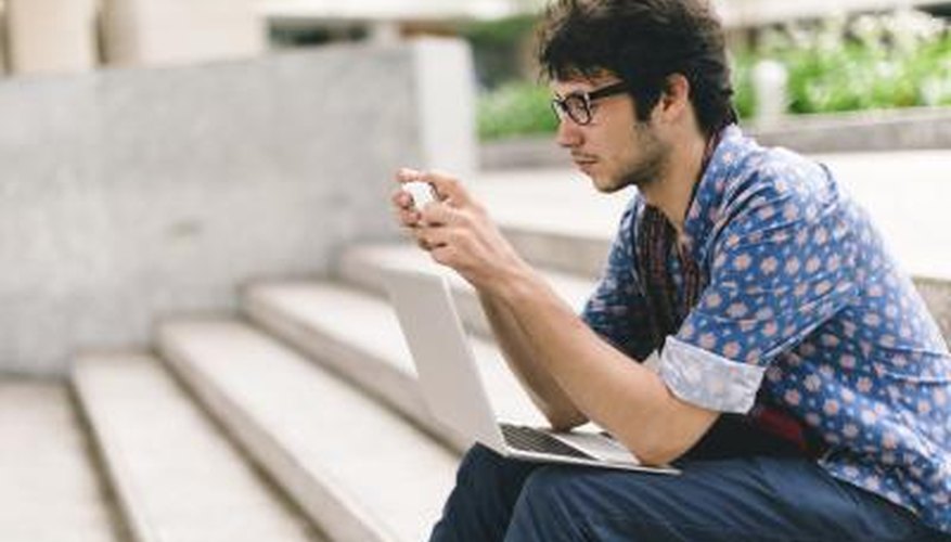 Student sitting on university steps with laptop and smart phone