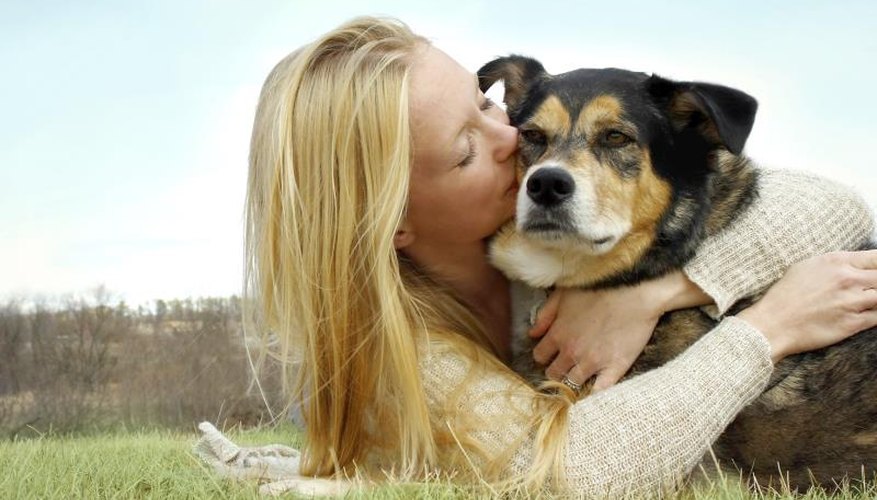 A woman hugging a dog while lying on grass.