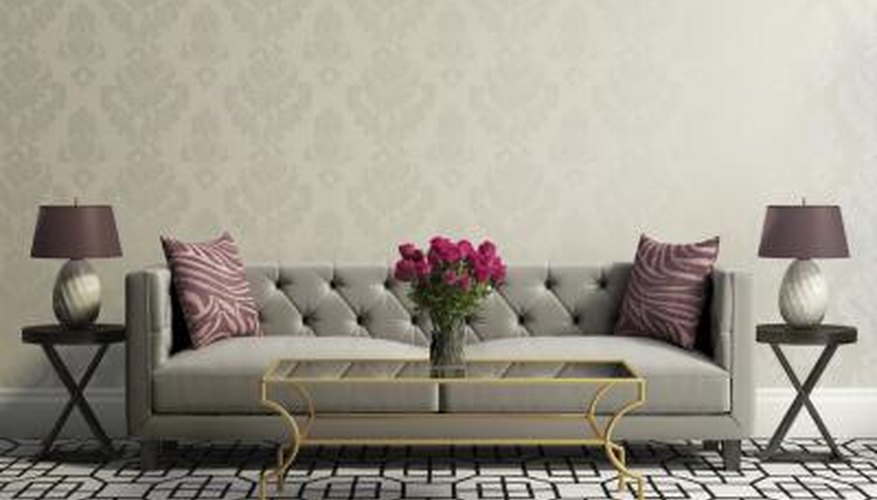 A vintage grey plush couch sits in between two matching classic wooden tables just wide enough to hold matching lamps. A vintage grey plush couch sits in between two matching classic wooden tables just wide enough to hold matching lamps.