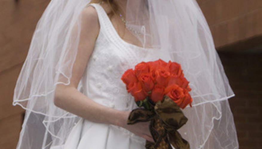 Novia tradicional con vestido blanco y velo, con un ramo de rosas rojas.