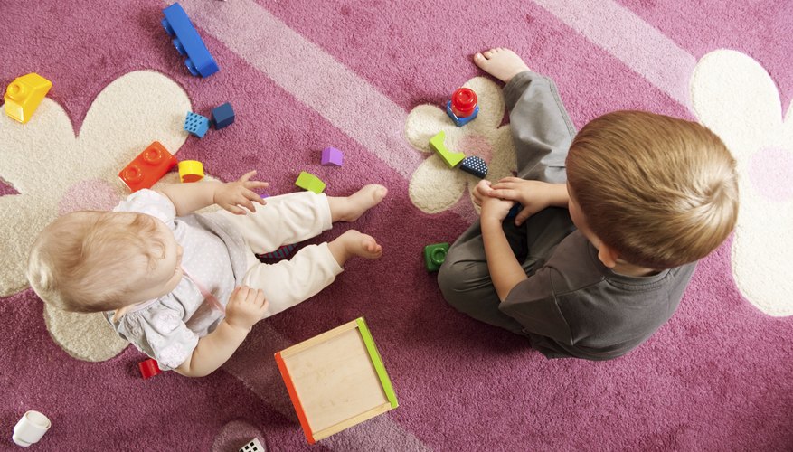 Young siblings playing with blocks together on the rug. Young siblings playing with blocks together on the rug.