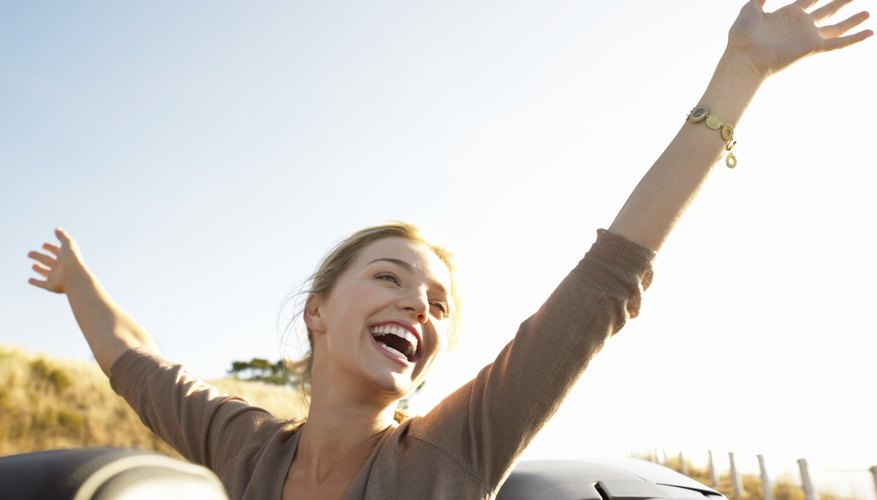 Young Woman Sits in the Back of a Convertible, Her Arms in the Air, Laughing With Joy