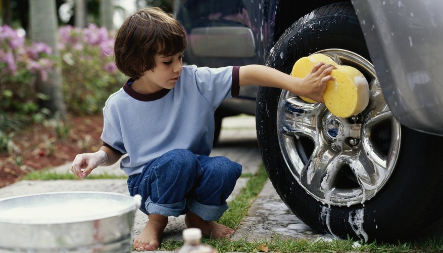 Boy (5-7) washing car wheel with sponge