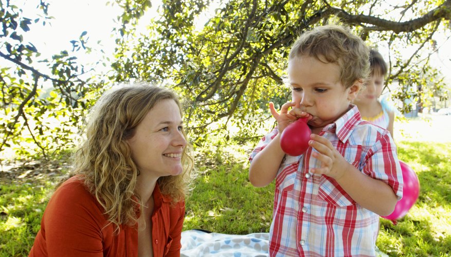 A woman in the park watching her children play with balloons. A woman in the park watching her children play with balloons.