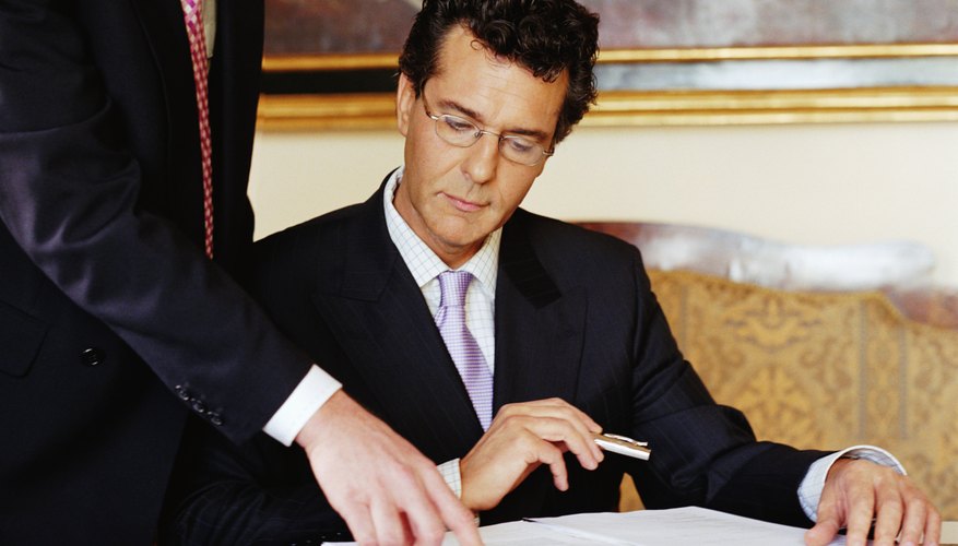 Mature businessman standing by colleague, pointing at papers on desk