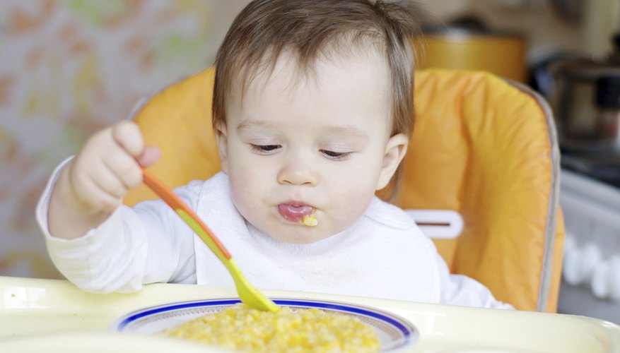 A 1 year old baby eating with a spoon. A 1 year old baby eating with a spoon.