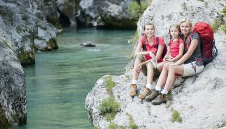 Photo Credit: Wojciech Gajda/iStock/Getty Images A mother and two daughters sit on a large rock next to a stream.