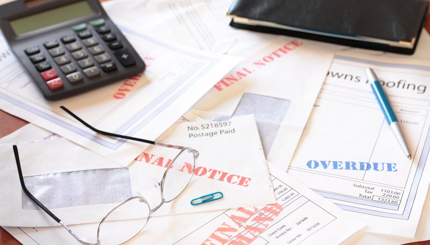 Stack of overdue bills on table with calculator and eye glasses.