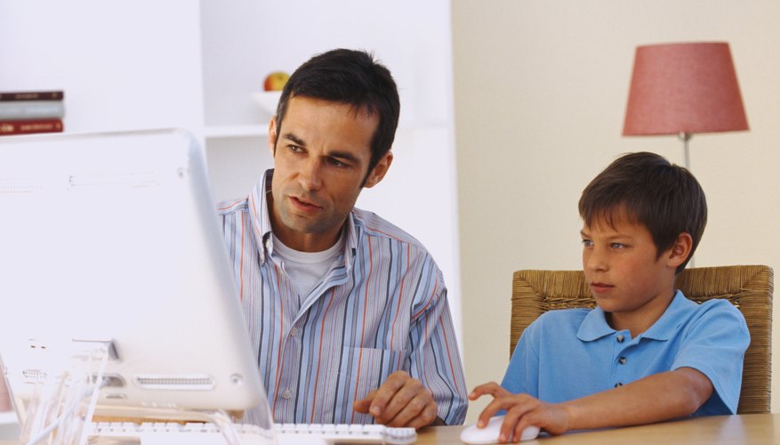 Mid adult man sitting at a table and working on a computer with his son (10-12)