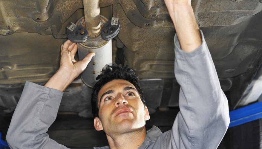 Low angle view of a male mechanic fixing an exhaust pipe on a car