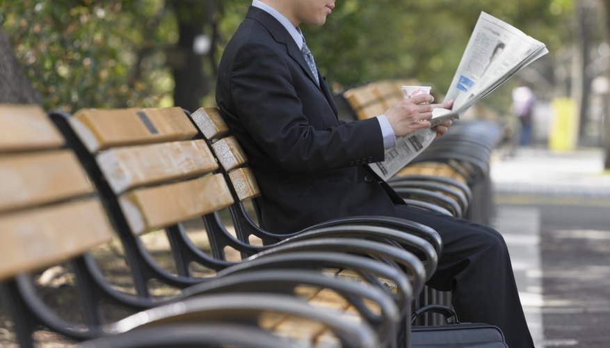Asian businessman reading newspaper on park bench